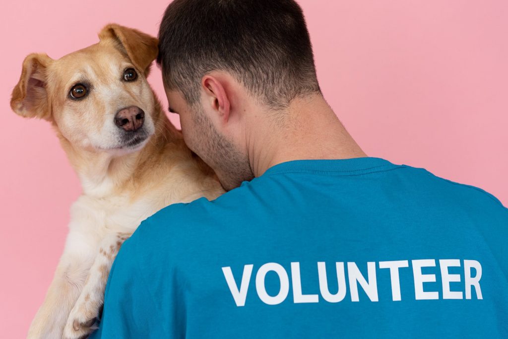 an animal shelter volunteer in a blue shirt holding a tan dog