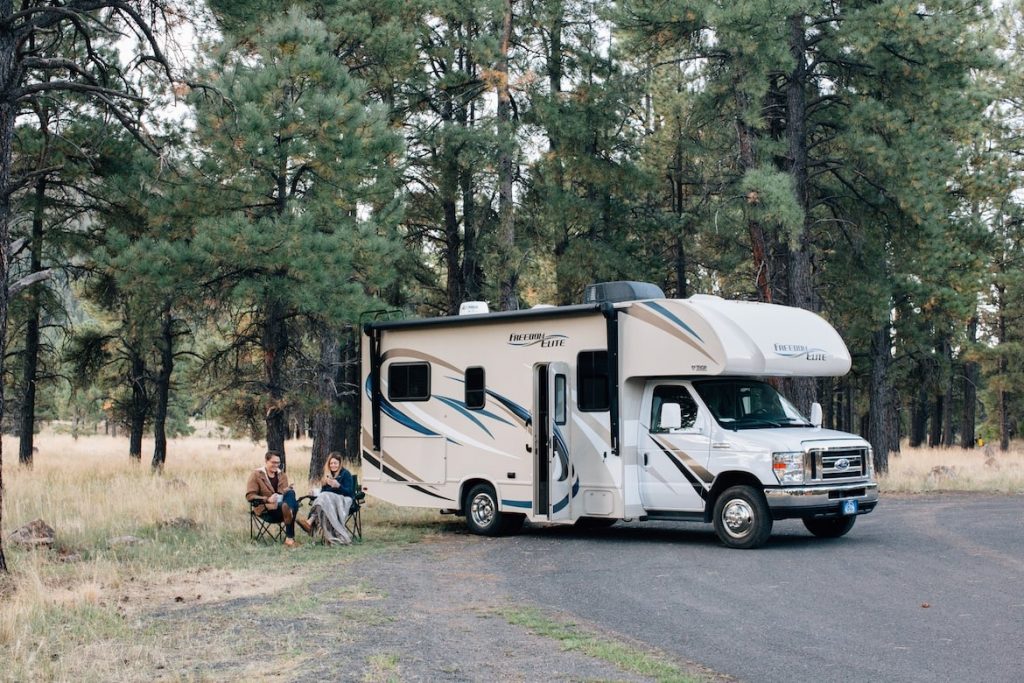 People Sitting Near a White Motorhome in a Forest